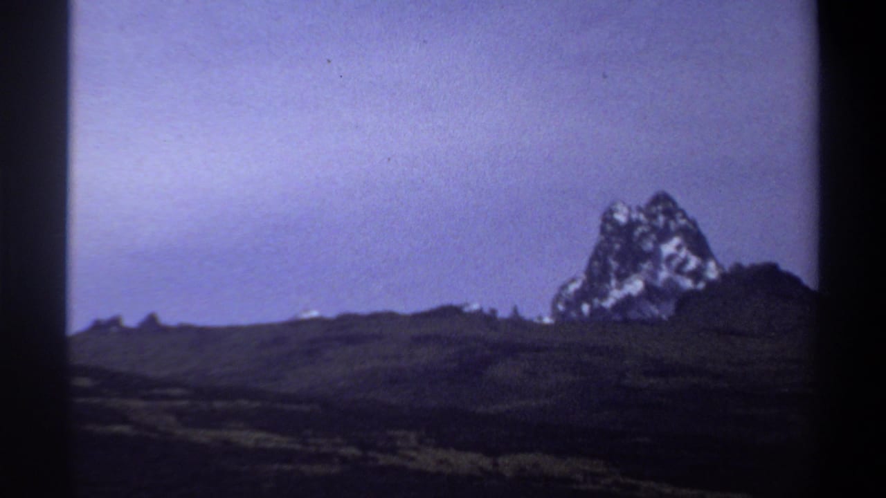 1969 Sudan home-movie frame showing dark plains and a rugged rock formation beneath a purple-blue sky.