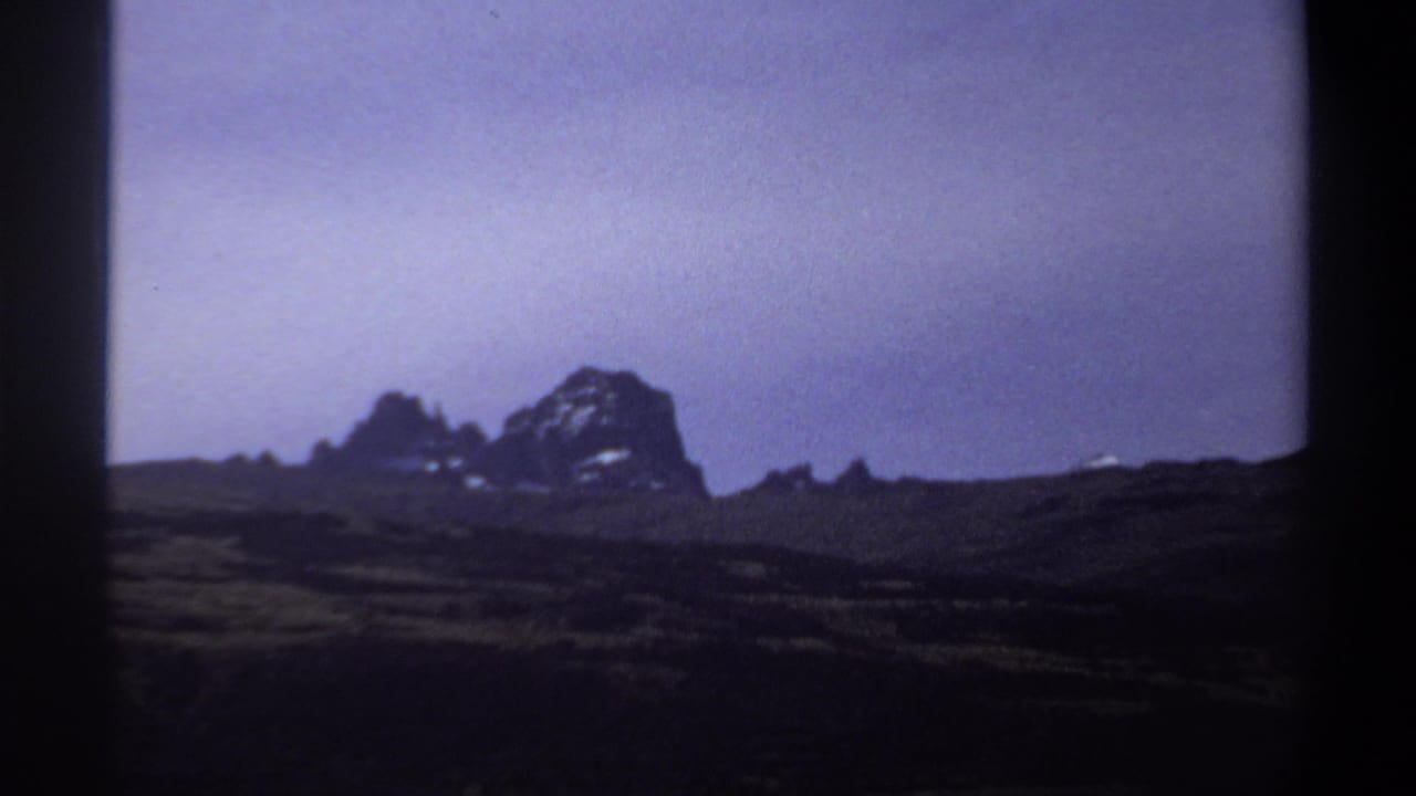 1969 Sudan landscape frame with low grassland, distant rugged rocks, and soft color-shifted 8mm texture.