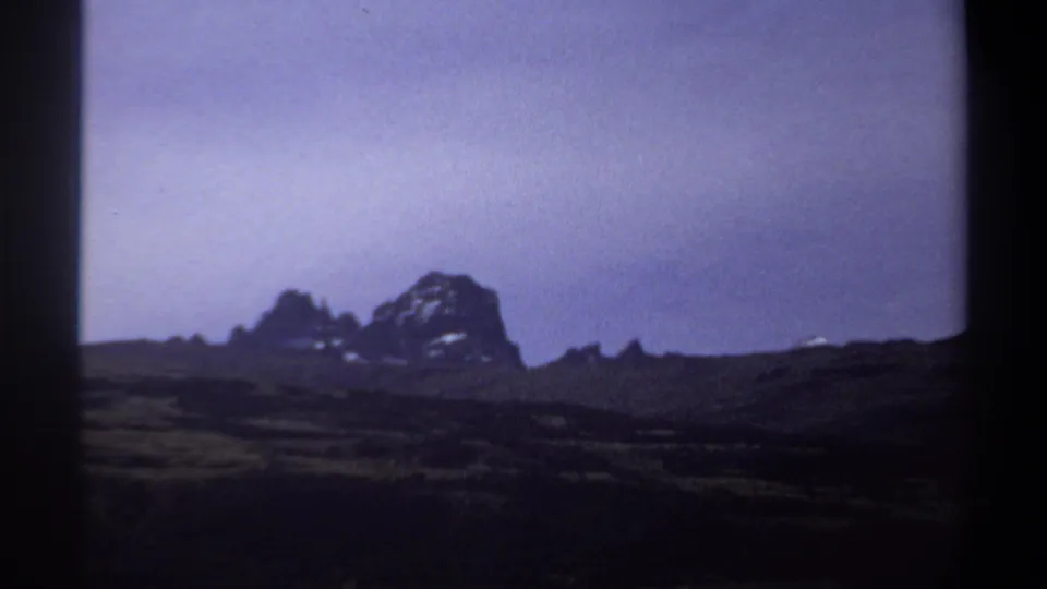 1969 Sudan landscape frame with low grassland, distant rugged rocks, and soft color-shifted 8mm texture.