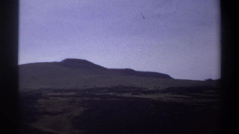 1969 Sudan landscape frame showing low rounded hills and dark open plains beneath a muted purple-blue sky.