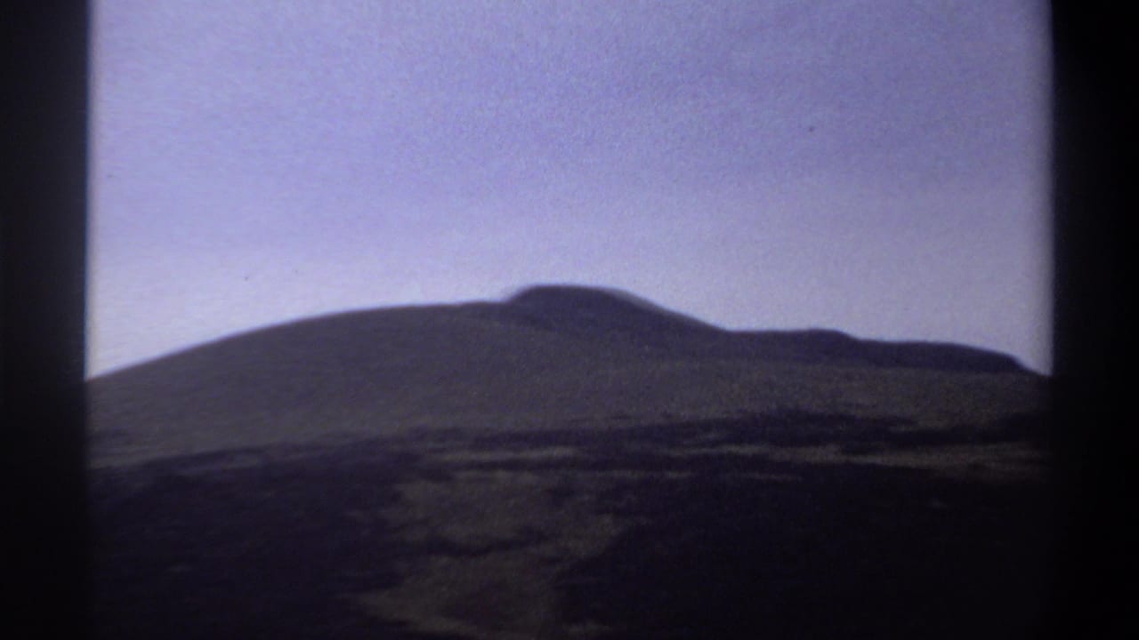 Dark hill silhouette beneath a pale sky, bordered by black film-frame edges.