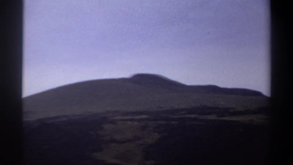 1969 Khartoum home-movie frame showing a distant dark hill line under a pale sky with strong 8mm border shadows.
