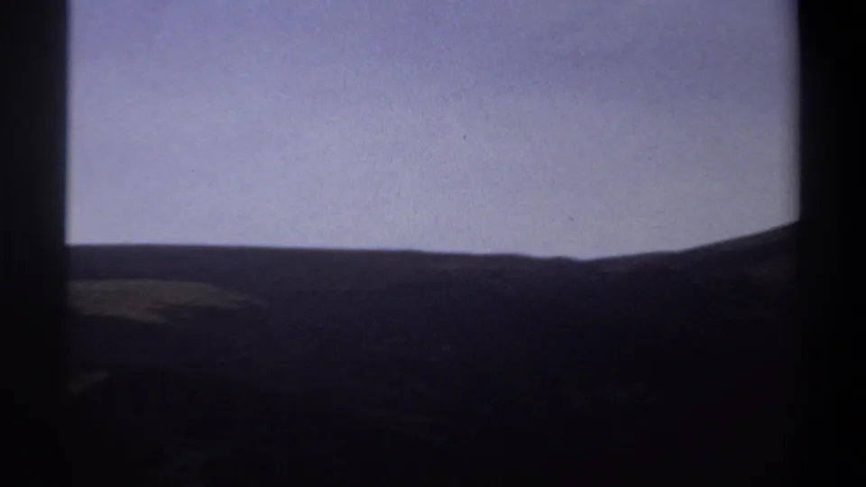 1969 Khartoum home-movie still showing a low dark ridgeline beneath pale sky and shadowed terrain.