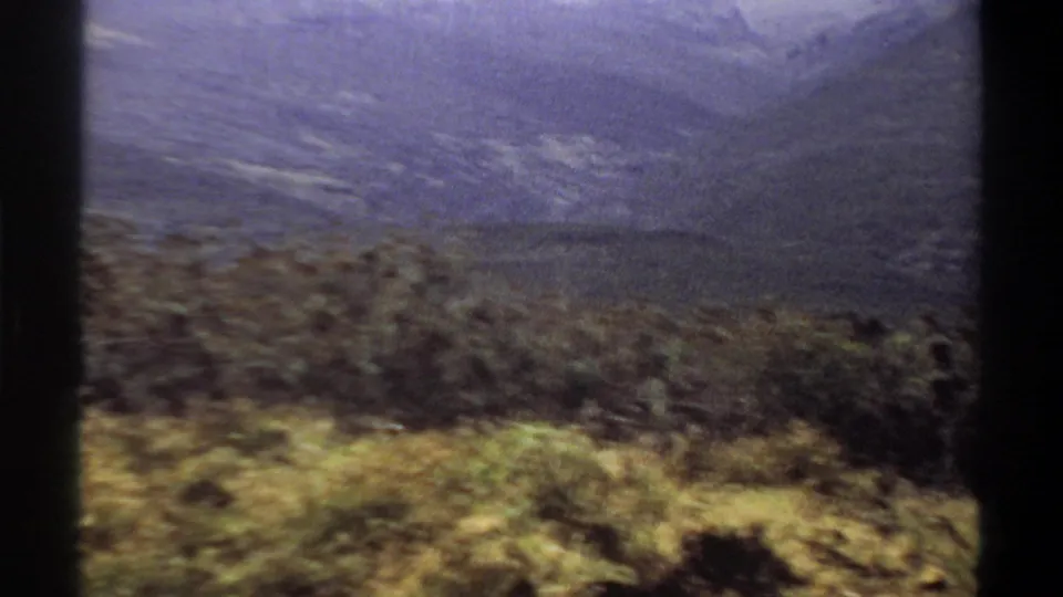 1969 Khartoum landscape frame with scrub vegetation in front of layered hills and a hazy blue-purple sky.