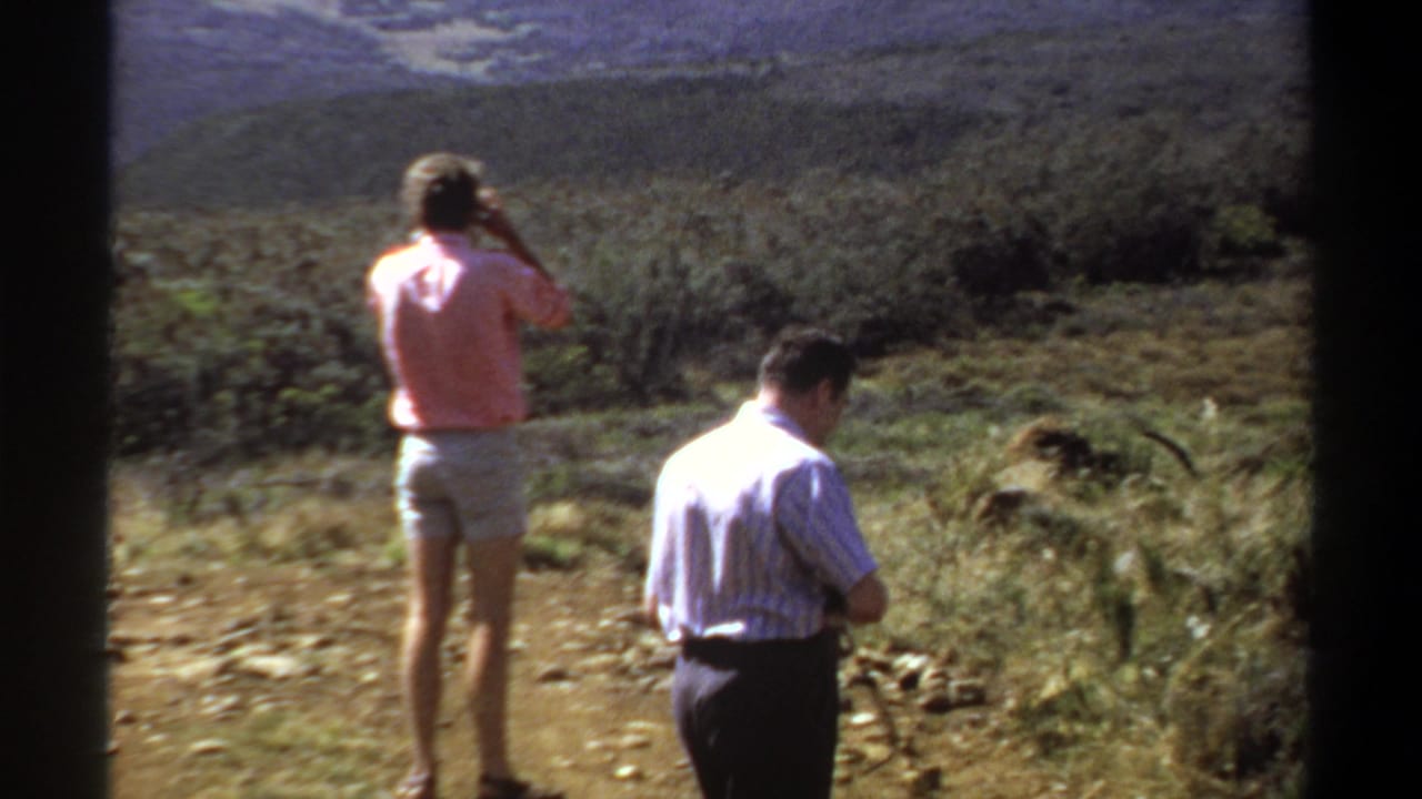 Two adults stand on rocky ground in a dry hillside landscape.