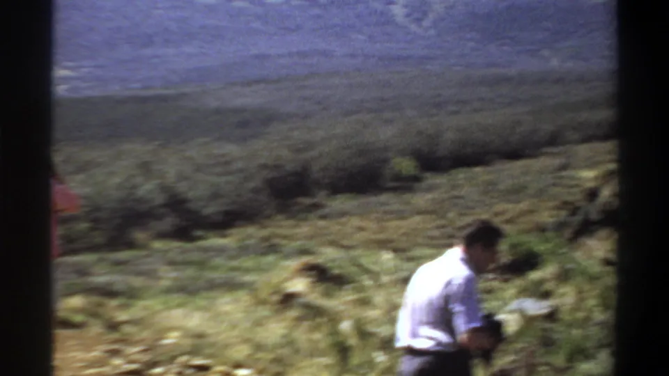 A soft, motion-blurred 8mm frame shows a man leaning in scrubby terrain in the metadata-listed Sudan setting.