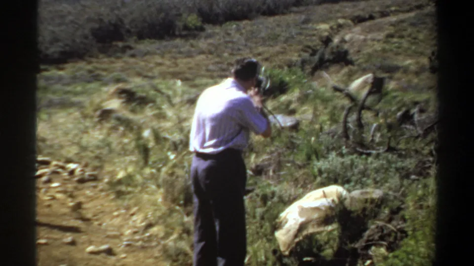 A man in a striped shirt appears to photograph or film the dry hillside landscape in 1969 Sudan home-movie footage.