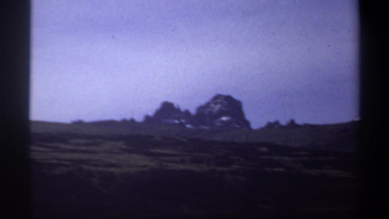 Low grassland and distant mountain shapes framed by dark film edges.