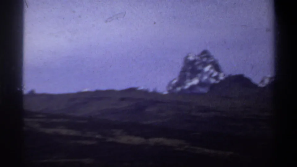 Sudan-labeled 1969 home-movie frame showing a rocky mountain mass beyond open, uneven grassland.