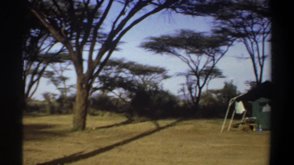 1969 Khartoum footage frame showing a small tent near trees on open grass, suggesting a casual campsite or rest area.