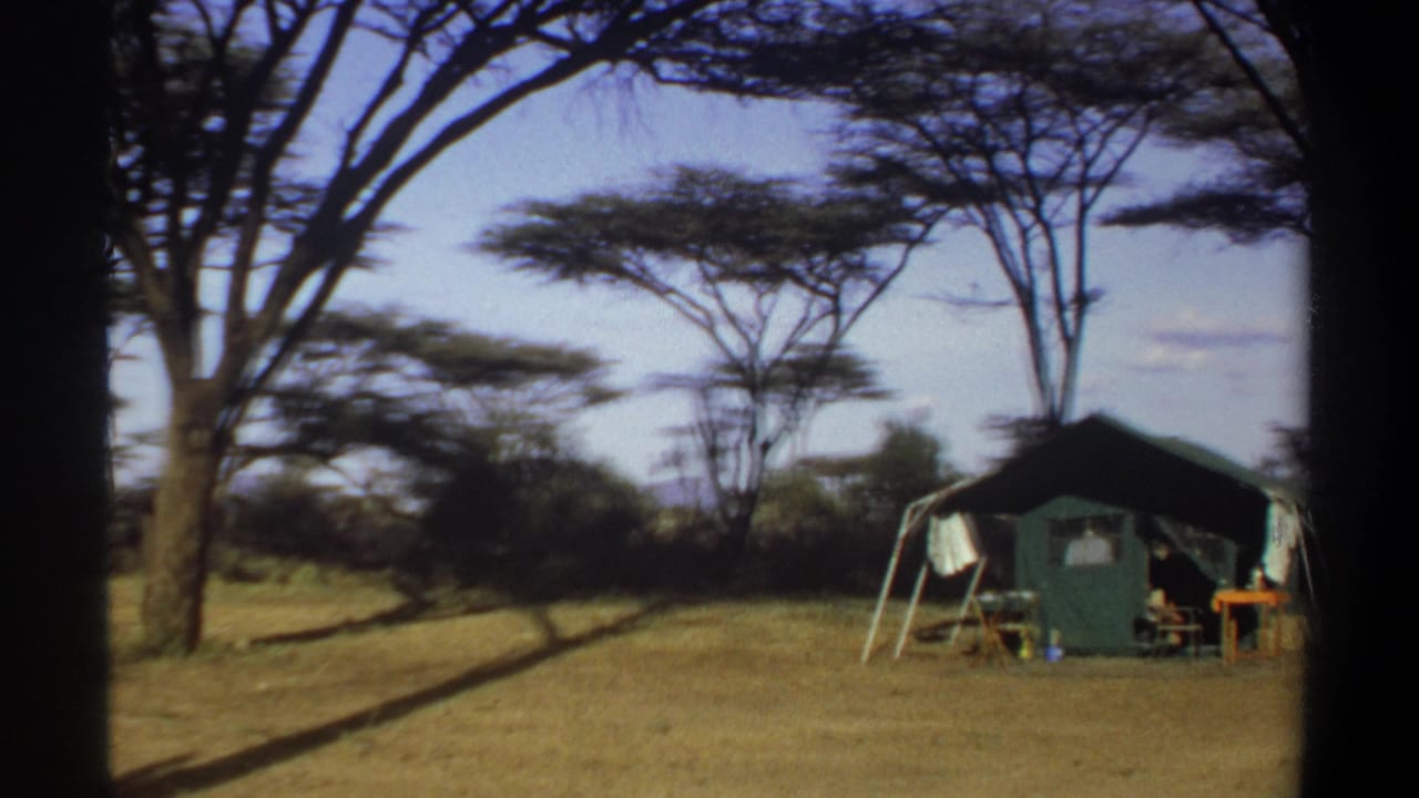 1969 Khartoum home-movie frame showing a green canvas camp tent under tall trees, with laundry and camp furniture outside.