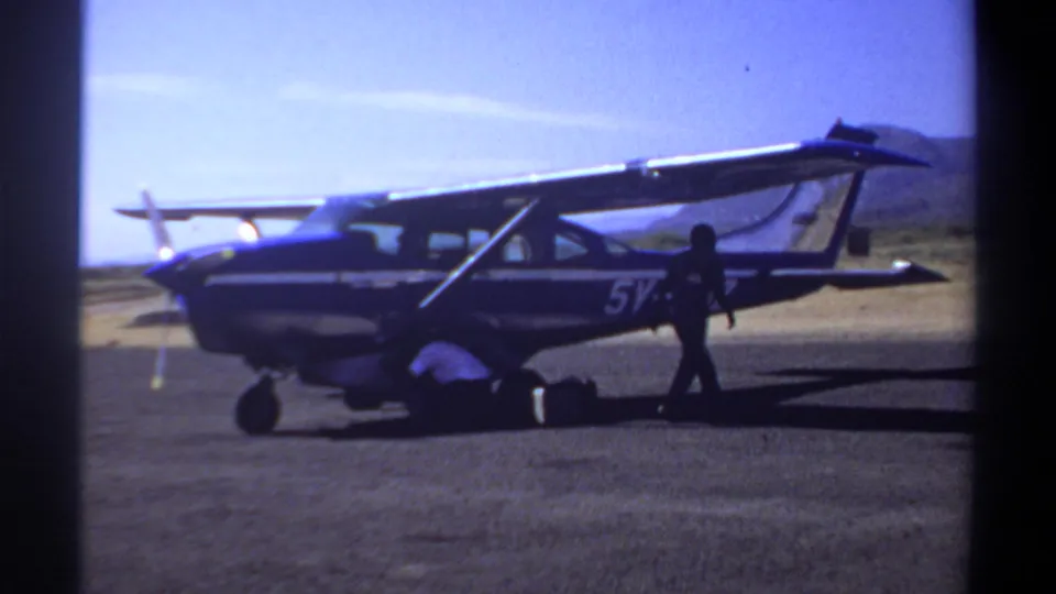 1969 Khartoum airfield view of a parked single-engine aircraft with servicing activity and a second person walking past.