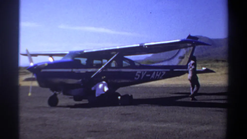 Blue and white aircraft marked 5V-AHZ on a Khartoum airfield in 1969, with personnel visible beside the landing gear and tail area.