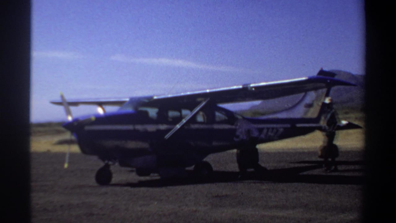 1969 Khartoum frame of a small aircraft on the runway, with adult figures moving near the wing and tail area.