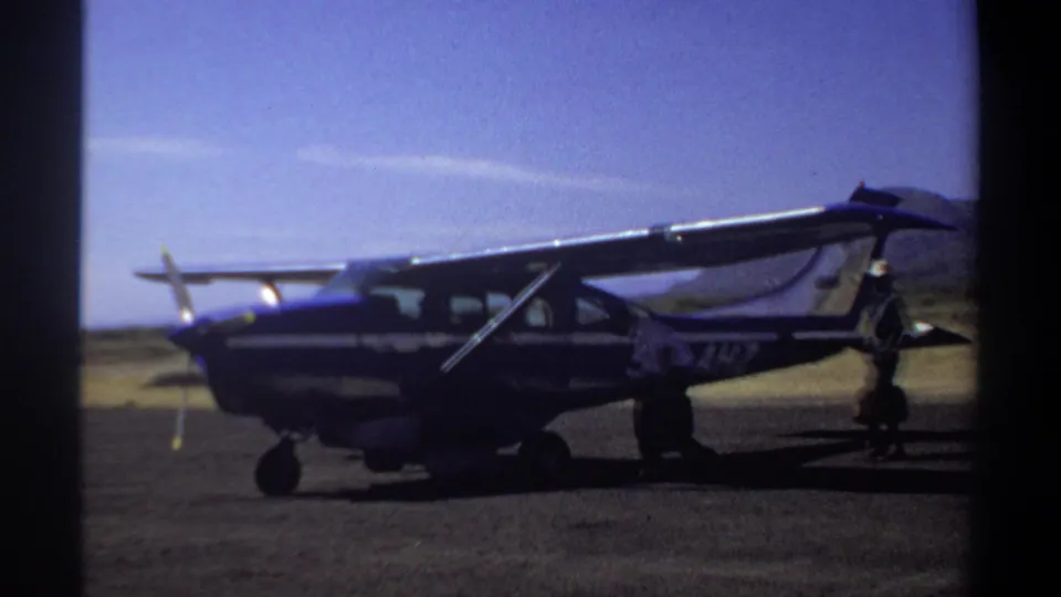 1969 Khartoum frame of a small aircraft on the runway, with adult figures moving near the wing and tail area.