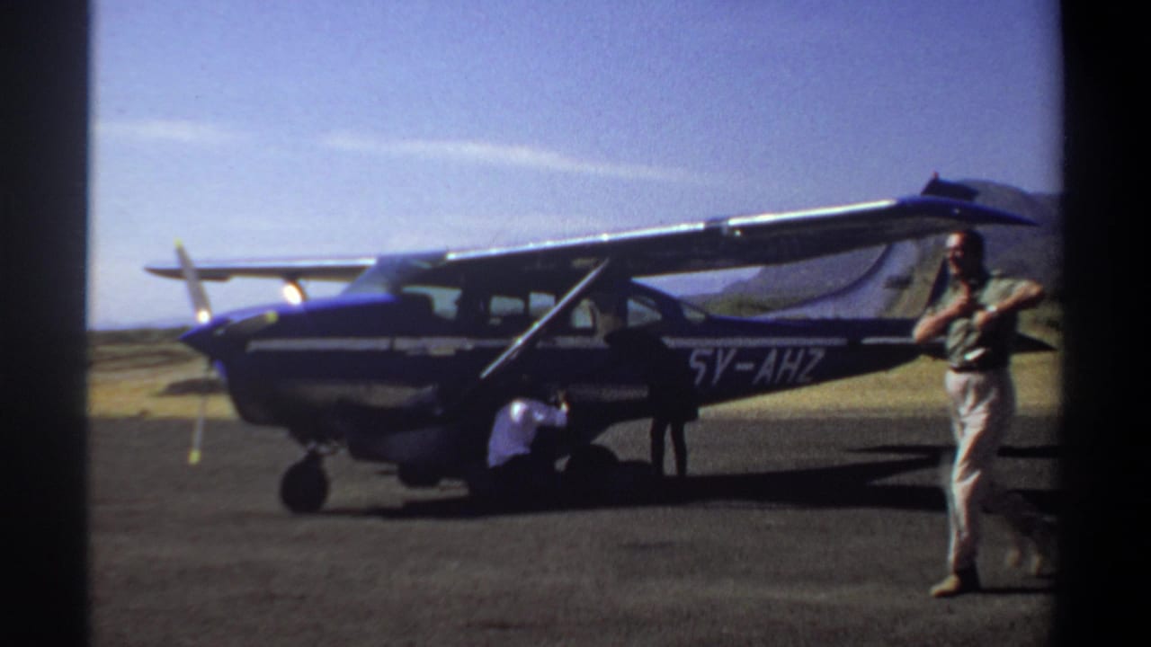 Small propeller plane with registration 5V-AHZ as a man in light clothing walks past in the foreground.