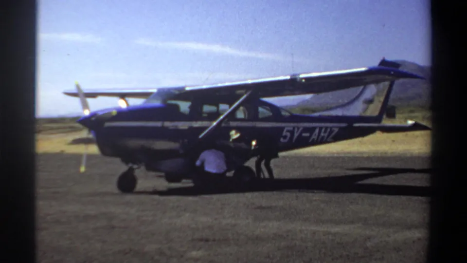 1969 Khartoum frame of a high-wing aircraft parked on a dusty runway as a person crouches beneath the fuselage.