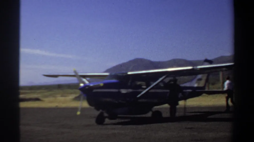 1969 Khartoum frame with the small propeller plane closer in view, showing the tail area, wing strut, and men partly visible on the airfield.