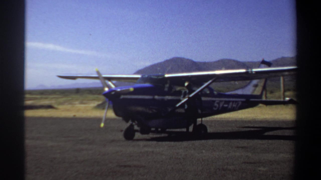 1969 Khartoum footage showing a blue single-engine propeller airplane parked on a sunlit airfield runway.