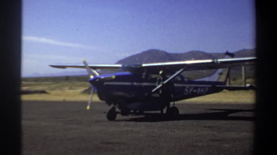 1969 Khartoum footage showing a blue single-engine propeller airplane parked on a sunlit airfield runway.