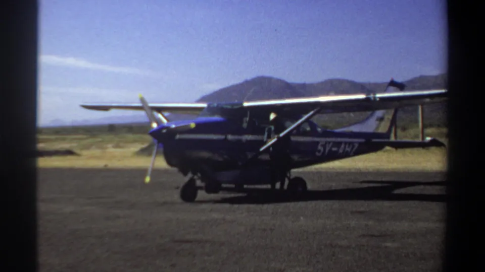 Blue aircraft parked on a Khartoum runway while a person appears beside the wing area in 1969 home-movie footage.