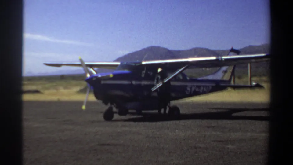 Blue single-engine propeller airplane remains parked on the Khartoum airfield with hills beyond the runway.