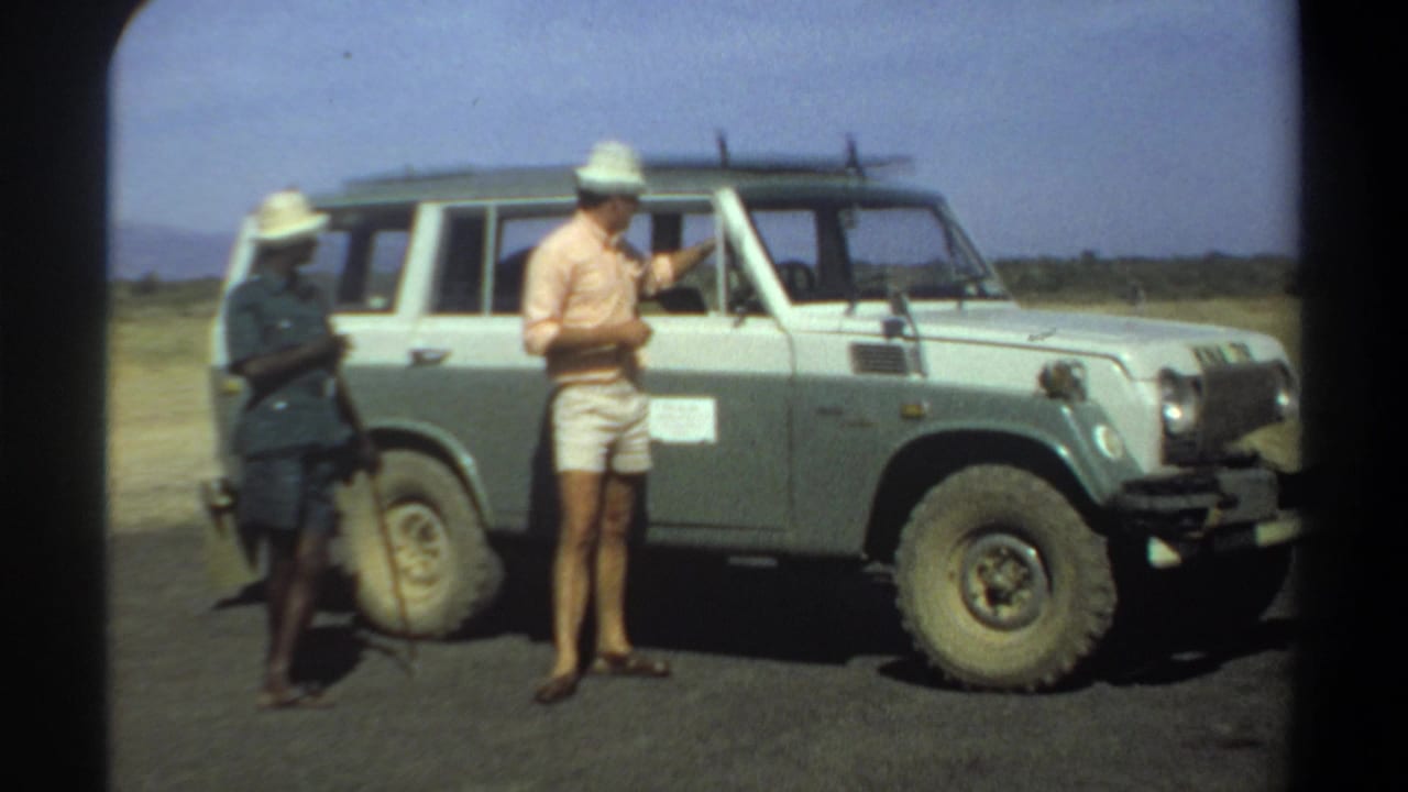 In 1969 Sudan footage, a civilian in shorts and a hat stands near a uniformed man beside a two-tone off-road vehicle.