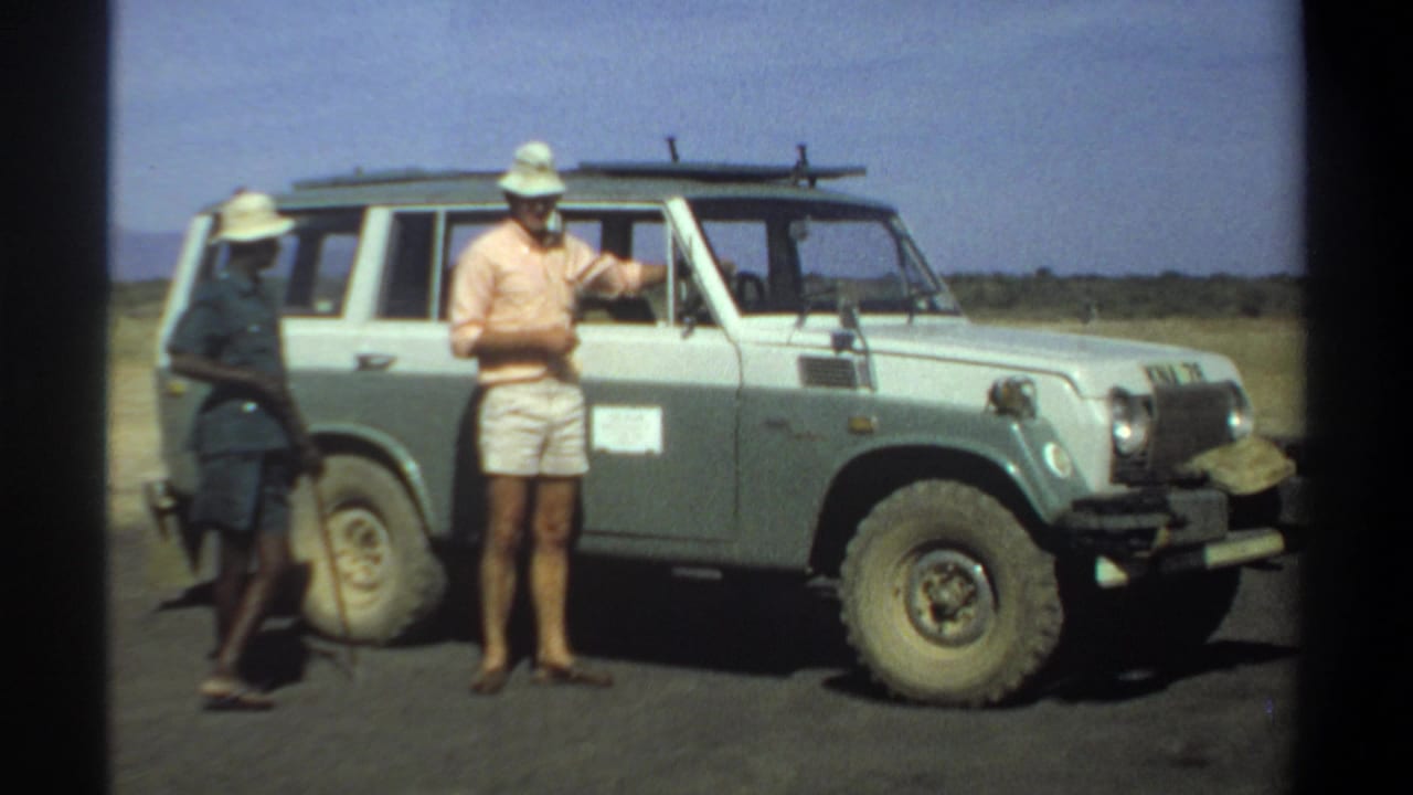 A civilian gestures near the driver's side of an off-road vehicle while a uniformed man stands behind him.