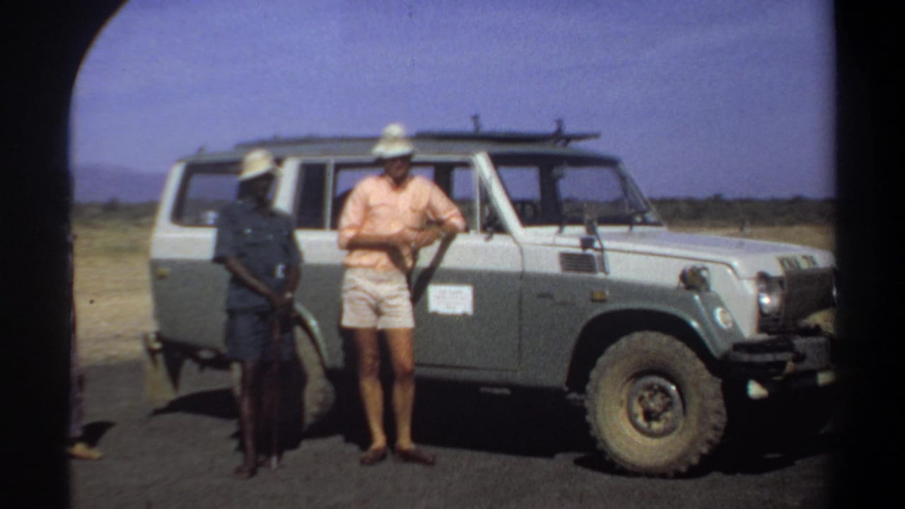 Two men stand near the open side of a pale off-road vehicle.