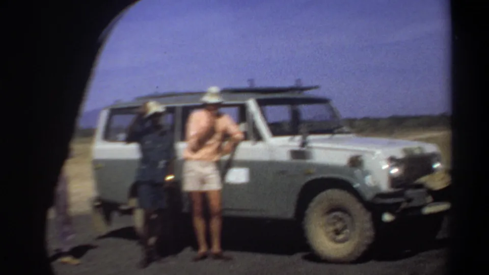 Khartoum, Sudan, 1969 home-movie frame showing three adult men beside a white off-road vehicle under a blue sky.