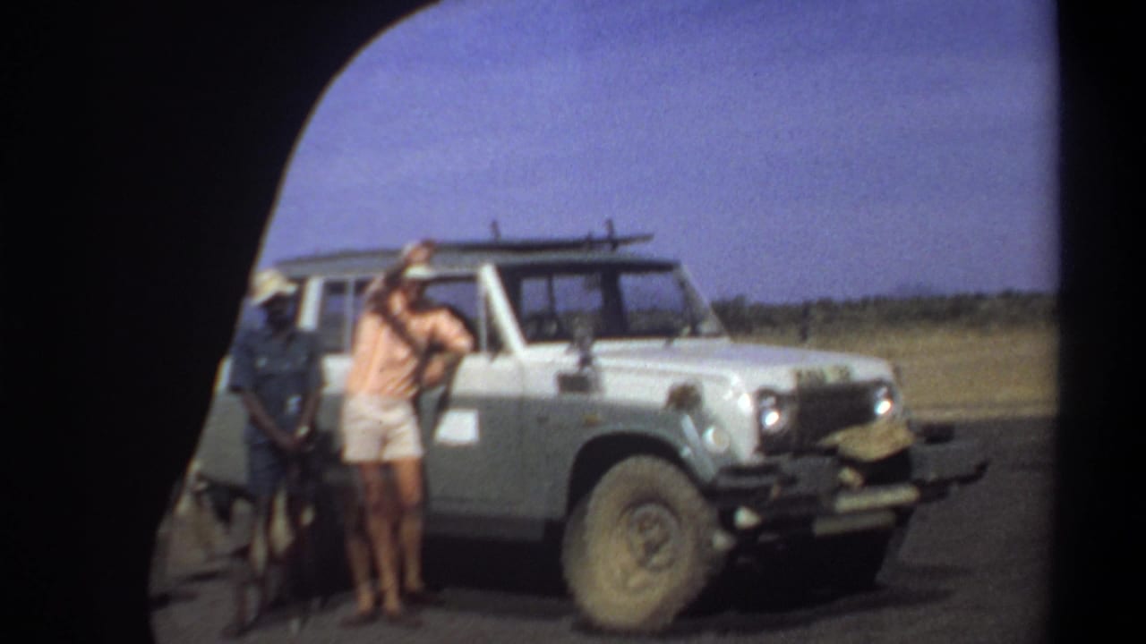 Khartoum, Sudan, 1969 frame with men standing near a white off-road vehicle on a roadside in open dry terrain.