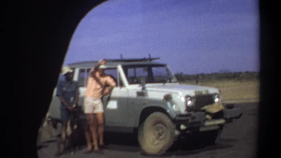 Khartoum, Sudan, 1969 frame with men standing near a white off-road vehicle on a roadside in open dry terrain.