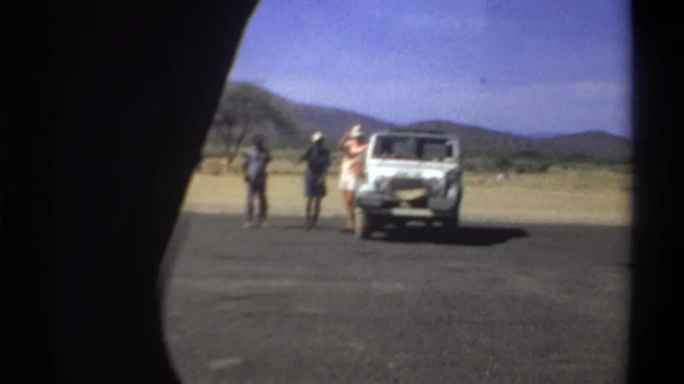 Wide 1969 Khartoum roadside view with three men near a white off-road vehicle, distant hills, and dry open ground.