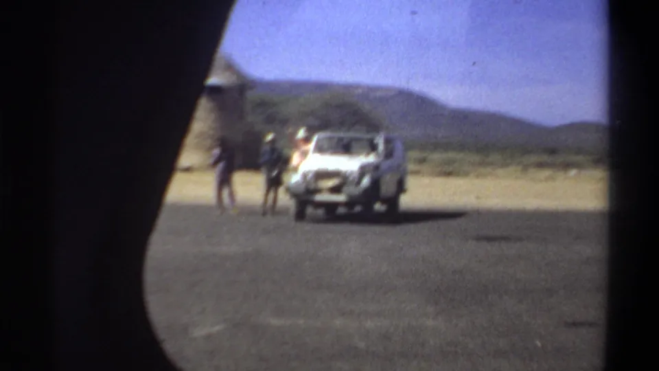 Distant Khartoum, Sudan, 1969 home-movie frame of three men and a white off-road vehicle in an arid roadside setting.