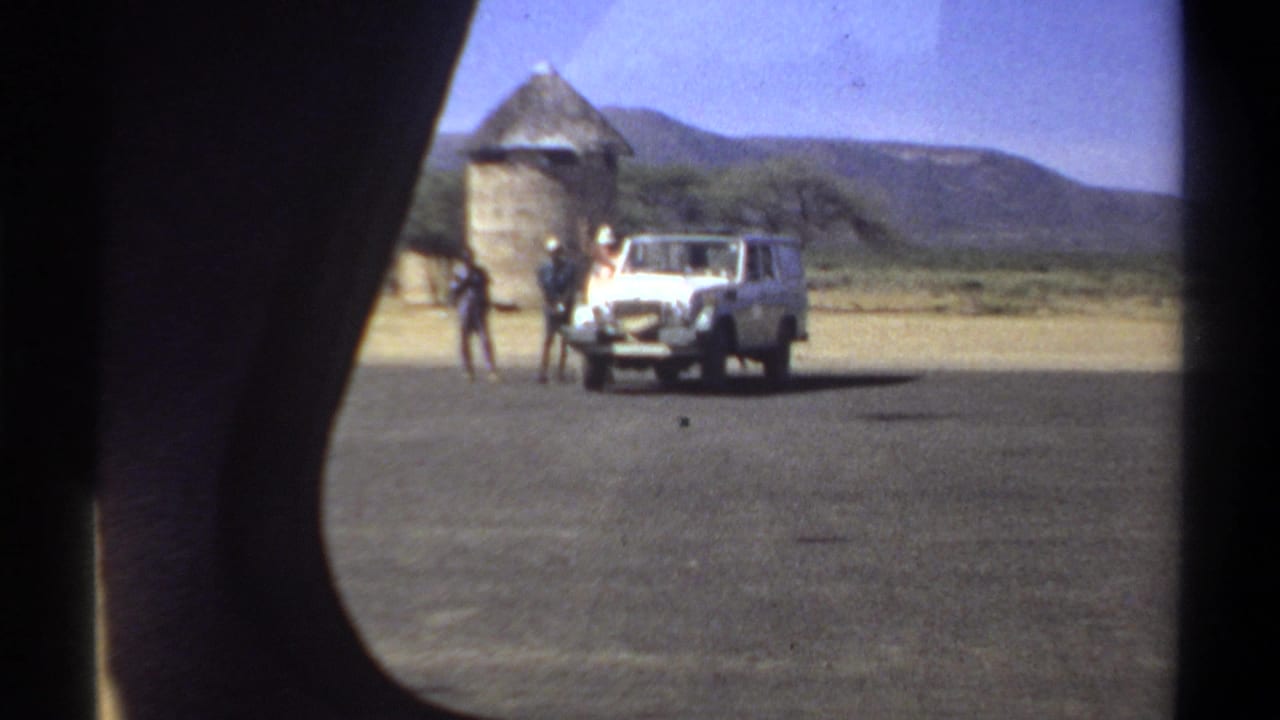 White utility vehicle parked near men and round thatched structures beside a paved area.