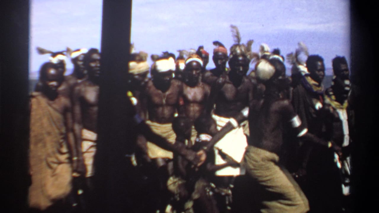 1969 Sudan 8mm frame showing a large outdoor group in wrapped cloth, headbands, armbands, and feathered headdresses.