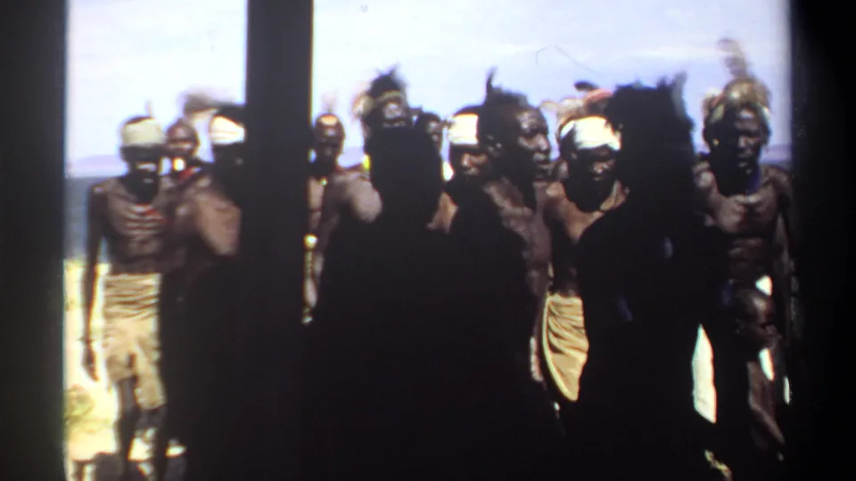 1969 Sudan 8mm frame with foreground silhouettes and a larger group behind in headbands, cloth wraps, and headdresses.
