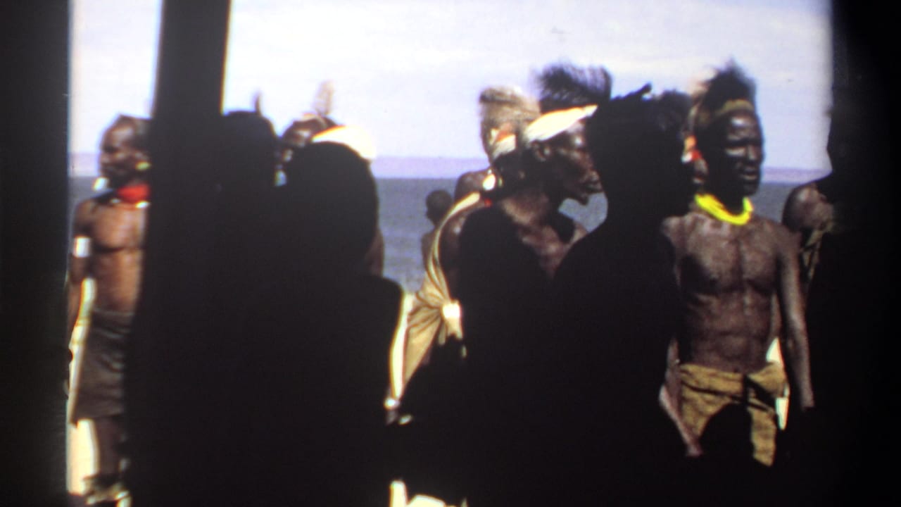 1969 Sudan home-movie frame with men in traditional dress moving near a shoreline, partly obscured by dark figures in the foreground.