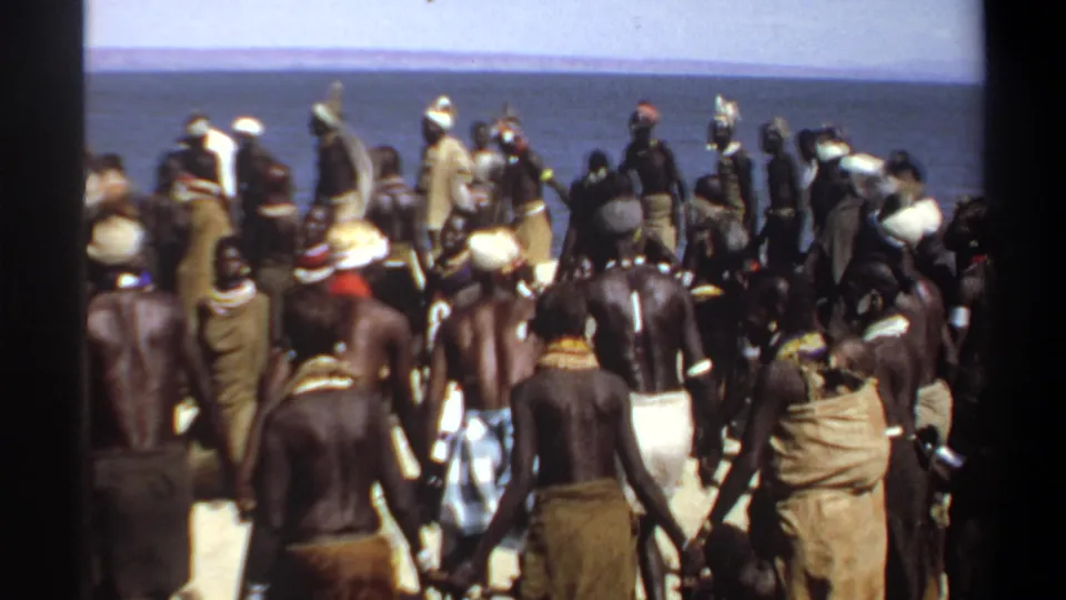 1969 Khartoum, Sudan frame of a crowded beach gathering, with figures in wraps and head coverings moving in bright sun.