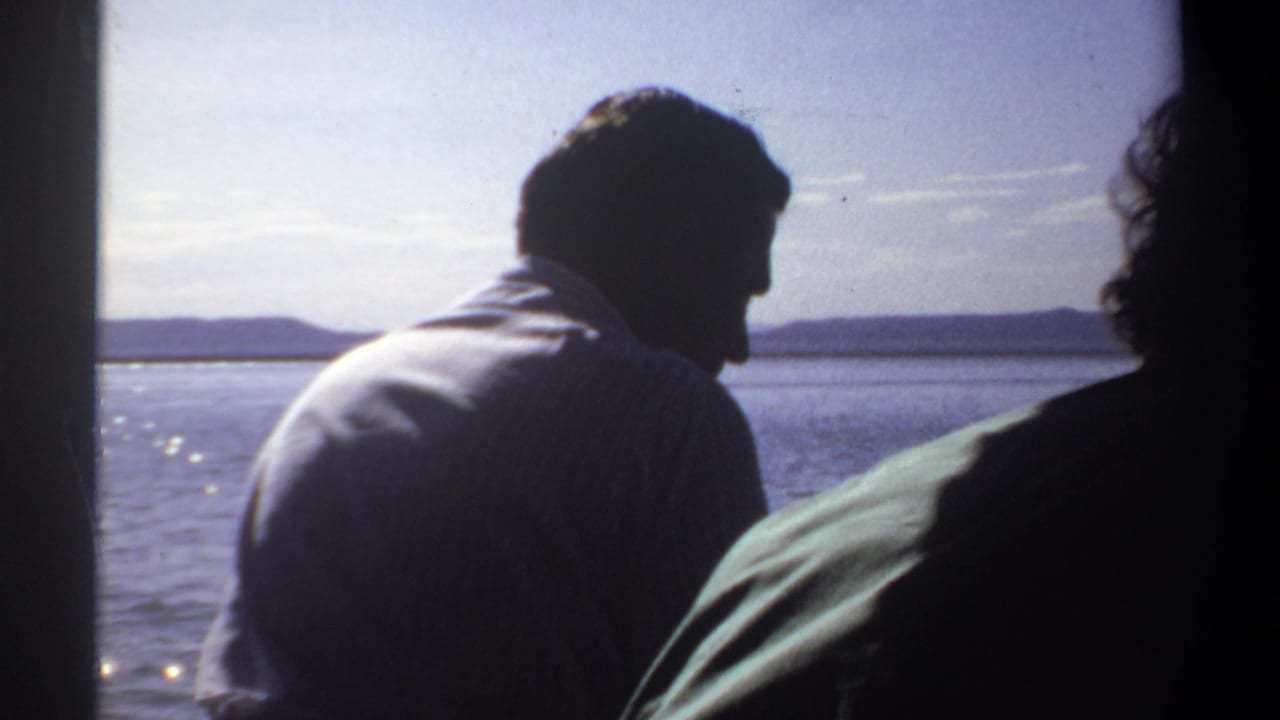 1969 Sudan home-movie frame showing two silhouetted men in a small boat against bright water and distant shoreline.