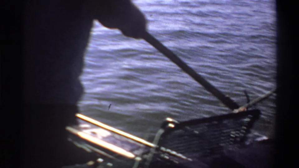 Backlit 1969 Sudan boat scene with a standing figure handling fishing gear beside rippled water.
