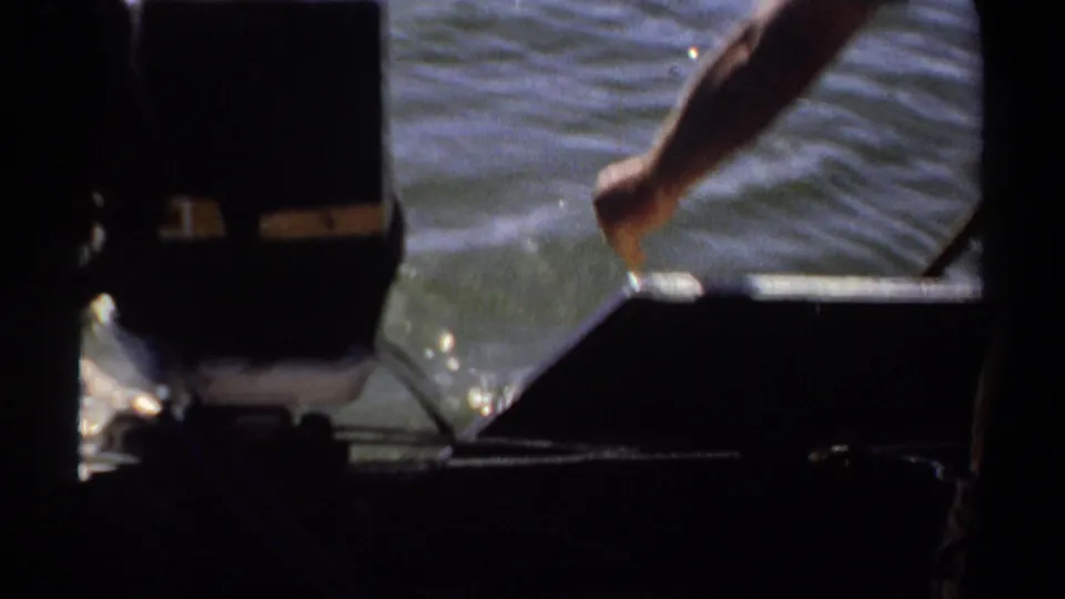 1969 Khartoum home-movie frame showing the stern area, an outboard motor, and a passenger's arm over sunlit water.