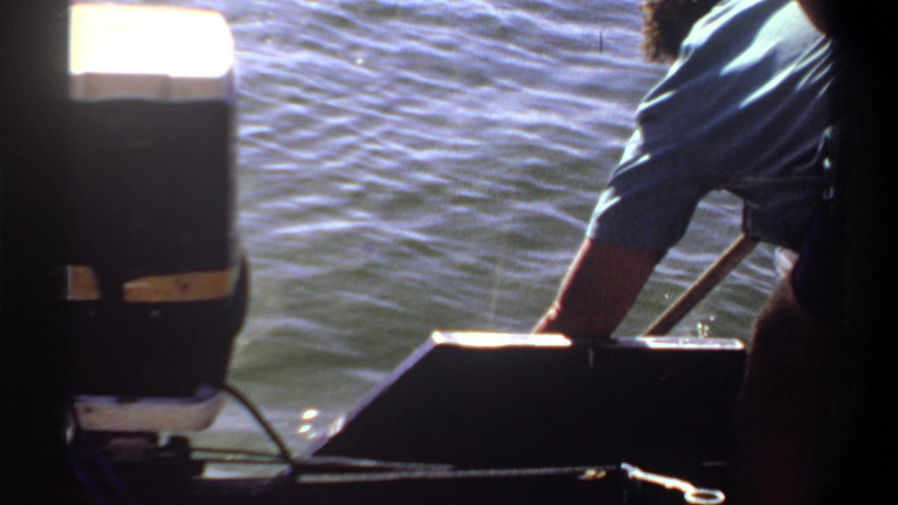 Boat motor and leaning man appear in front of bright rippling water.