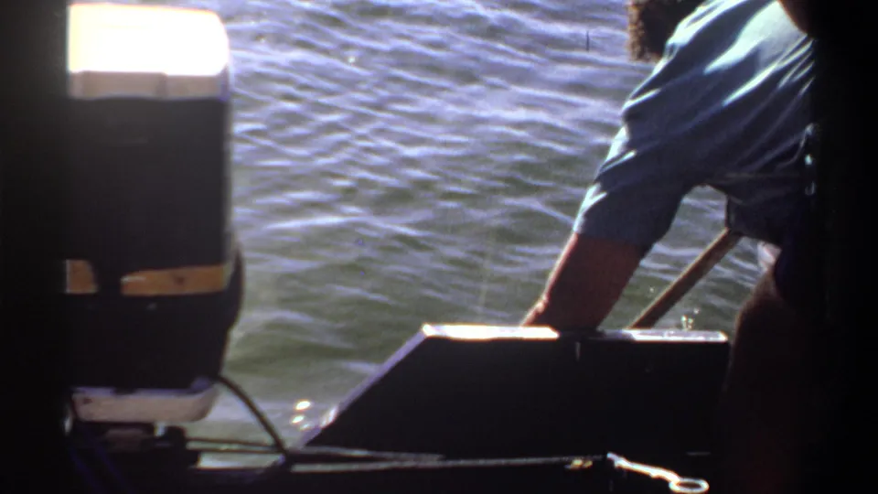 1969 Khartoum 8mm frame with the boat motor in the foreground and a man in a blue shirt leaning down toward the water.