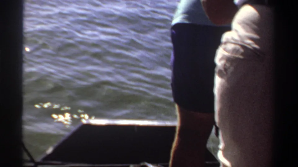 1969 Khartoum home-movie frame showing two adults on a small boat, one partly cropped, with rippling water in the background.
