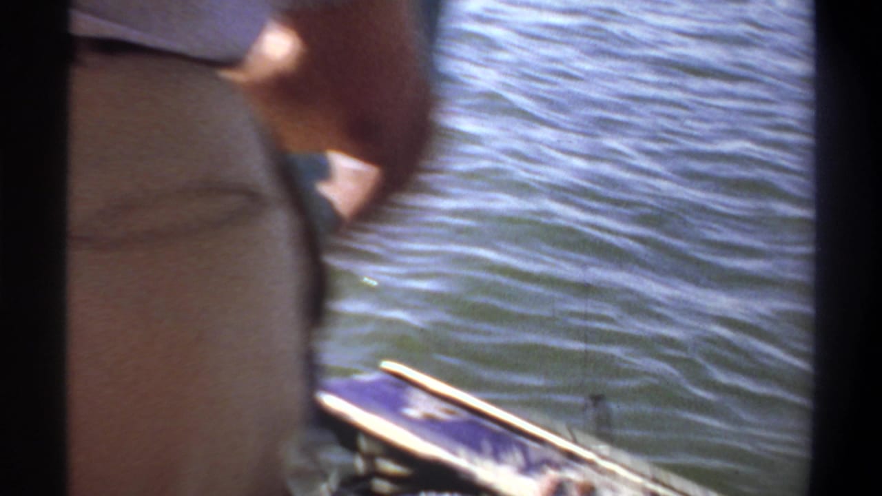 1969 Khartoum home-movie frame showing cropped adults on a small boat near rippling water, with the boat edge and partial motor in view.