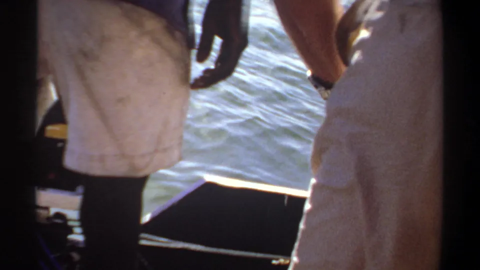 1969 Khartoum home-movie frame showing cropped adults on a small boat with bright water, a dark central frame, and boat interior details.