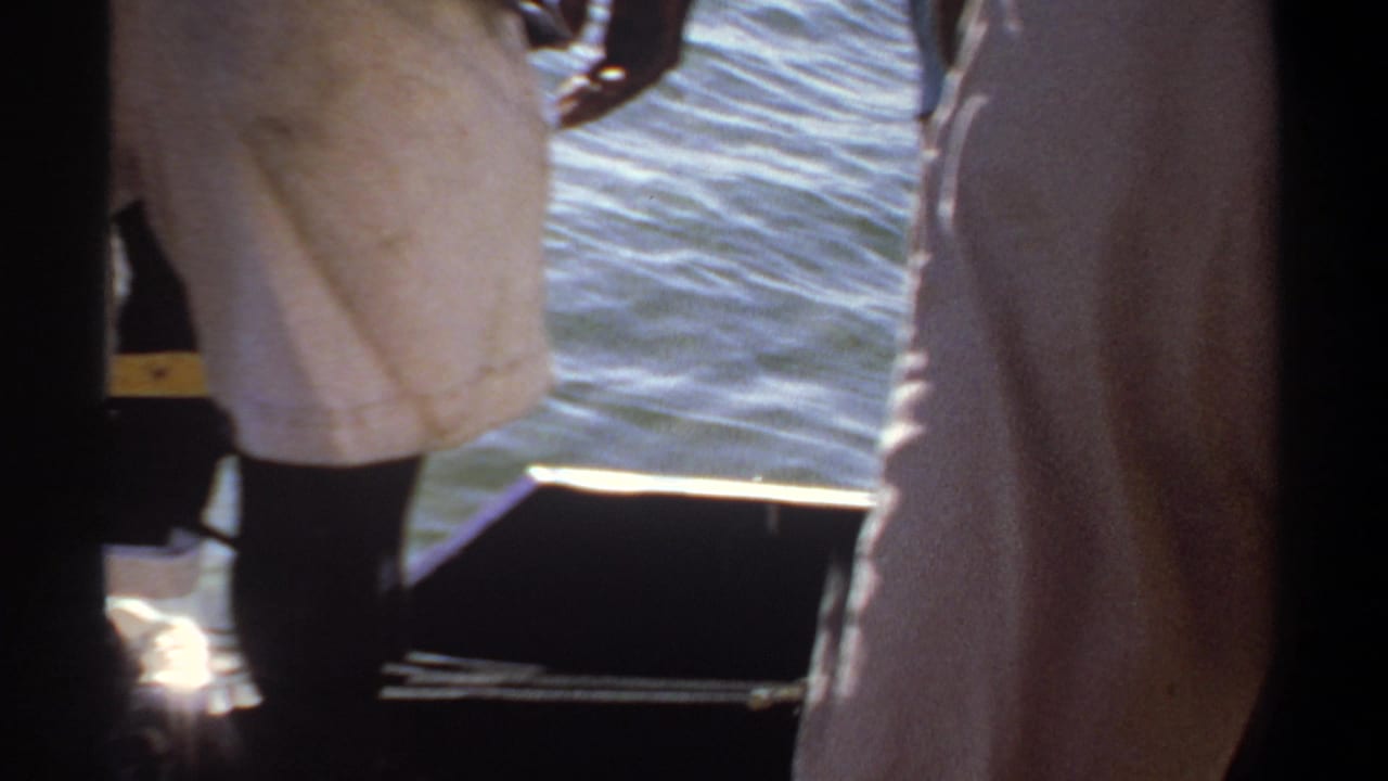 Partial view of men on a boat with sunlit water behind them.