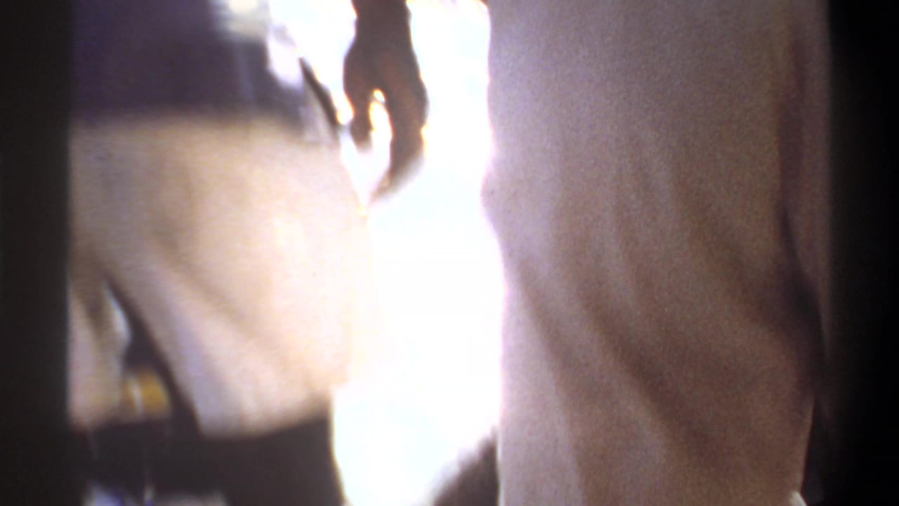 1969 Khartoum home-movie frame showing cropped adult legs near a boat, with intense sunlight reflecting from the water.