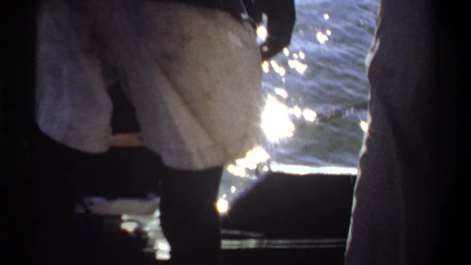 1969 Khartoum footage frame with a person in white shorts stepping near a boat edge as bright water shimmers behind.